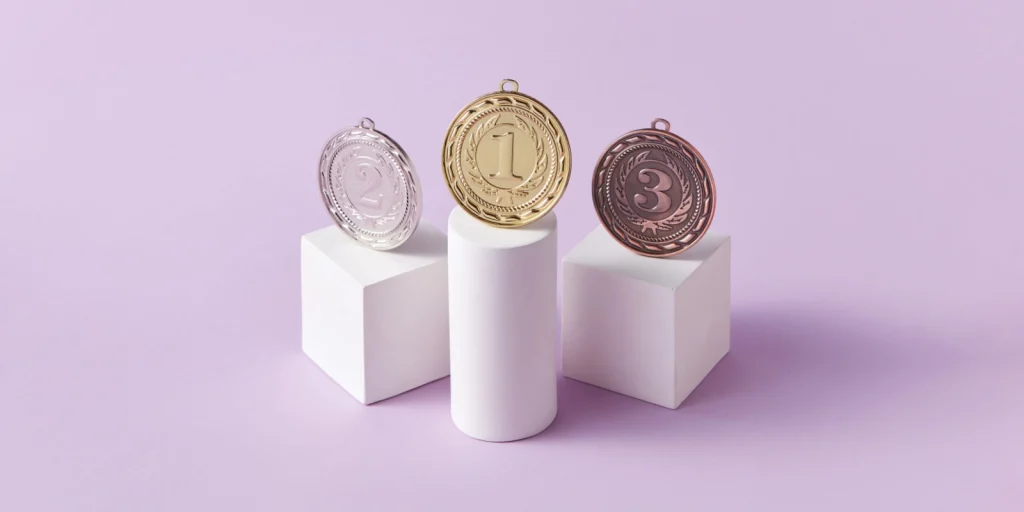 B2B marketing consistency diagram illustrating how strategic repetition builds industry category leadership and visibility for growth-focused brands. Image of three medals on stands with a pale lilac background.